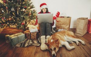 Woman with Santa hat and computer under Christmas tree