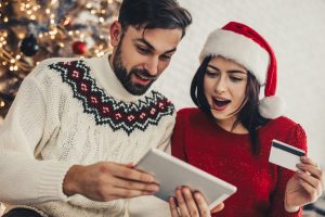 couple hold tablet and credit card while shopping in holiday sweaters