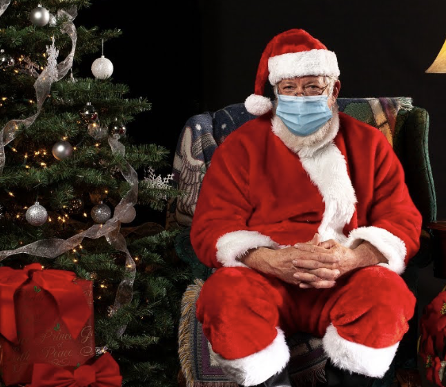 Santa with a mask on sitting next to Christmas tree