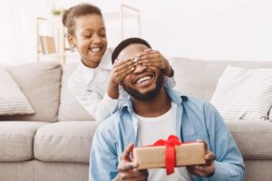 Father and child on Father's Day with gift. Father's day advertising and gift trends 2022. Happy daughter congratulating dad and giving present at home