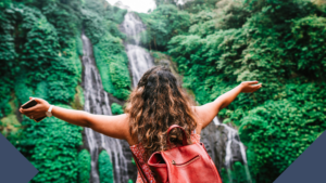 woman hands wide in front of waterfall wearing backpack for travel trends advertising trends travel and pride